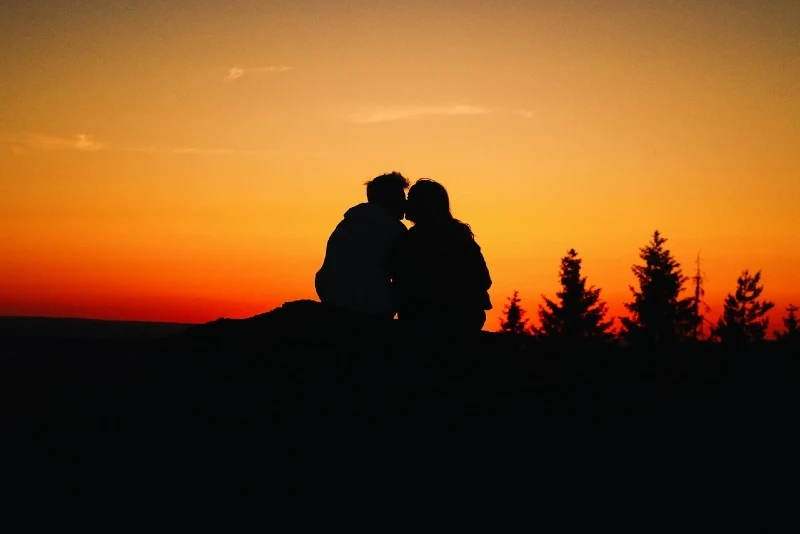 man and woman kissing while sitting outdoor during sunset