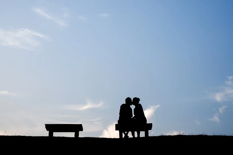 man and woman kissing while sitting on bench