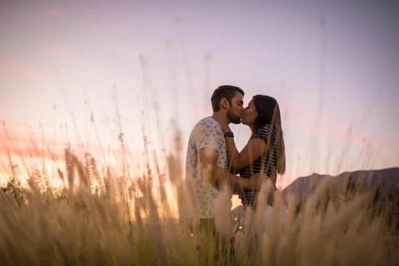 man and woman kissing on grass field