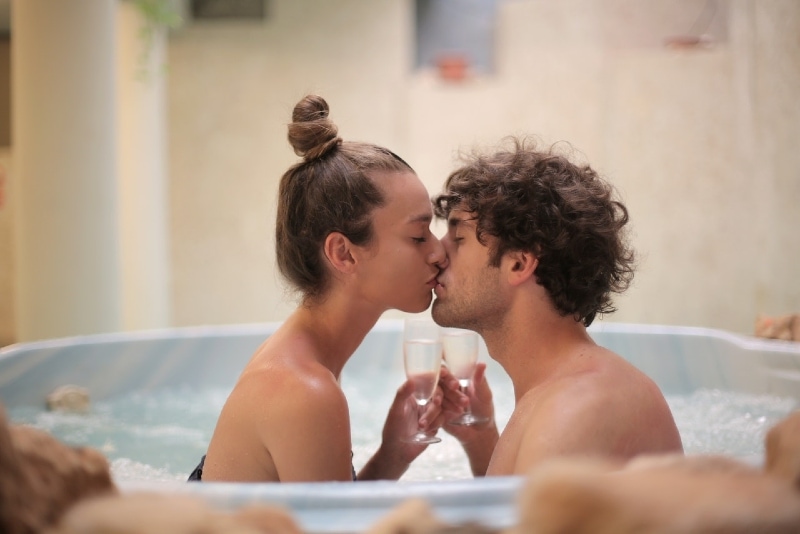 uomo e donna che si baciano nella vasca da bagno tenendo in mano bicchieri di champagne