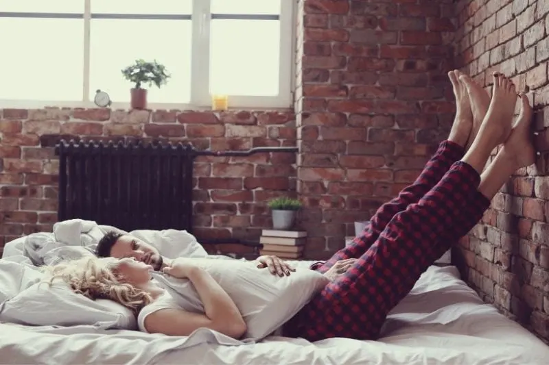 couple lying down in bed of an apartment room with feet on the brick walls