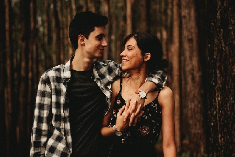 man and woman making eye contact while standing in forest