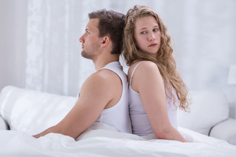 couple marital problem sitting back to back on the bed wearing white tank top