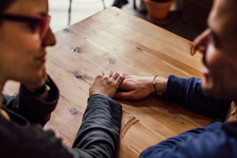 homem e mulher de mãos dadas sentados à mesa