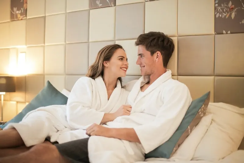 man and woman in white robes sitting on bed