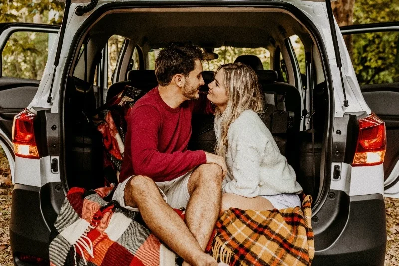 man and woman making eye contact while sitting on car's trunk
