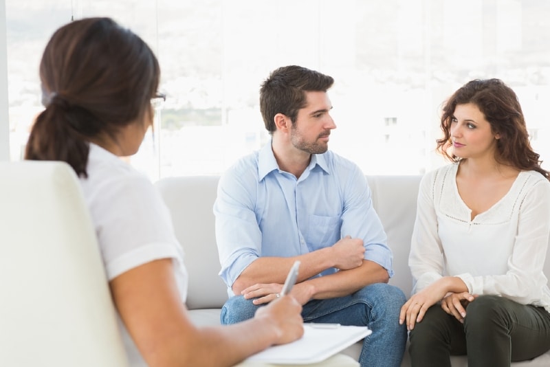 man and woman sitting on couch while talking to therapist