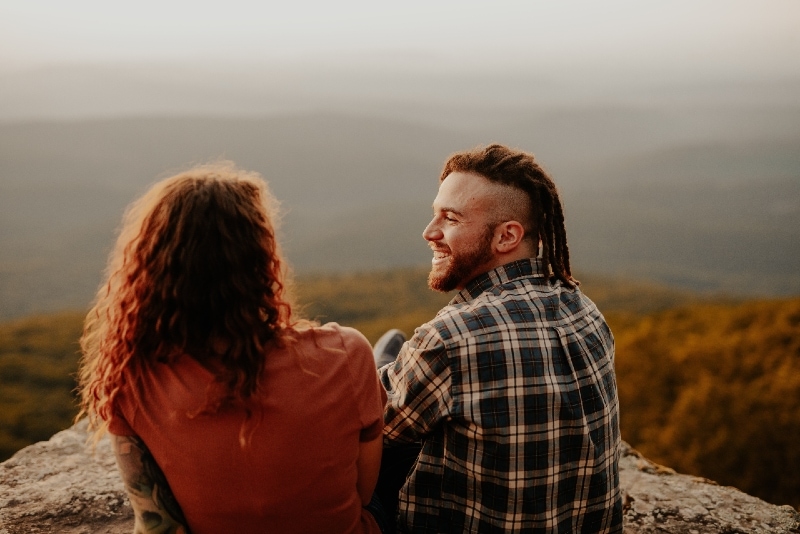 happy man in checked shirt and woman sitting on rock