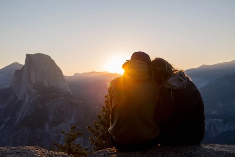 man and woman sitting on rock during sunrise