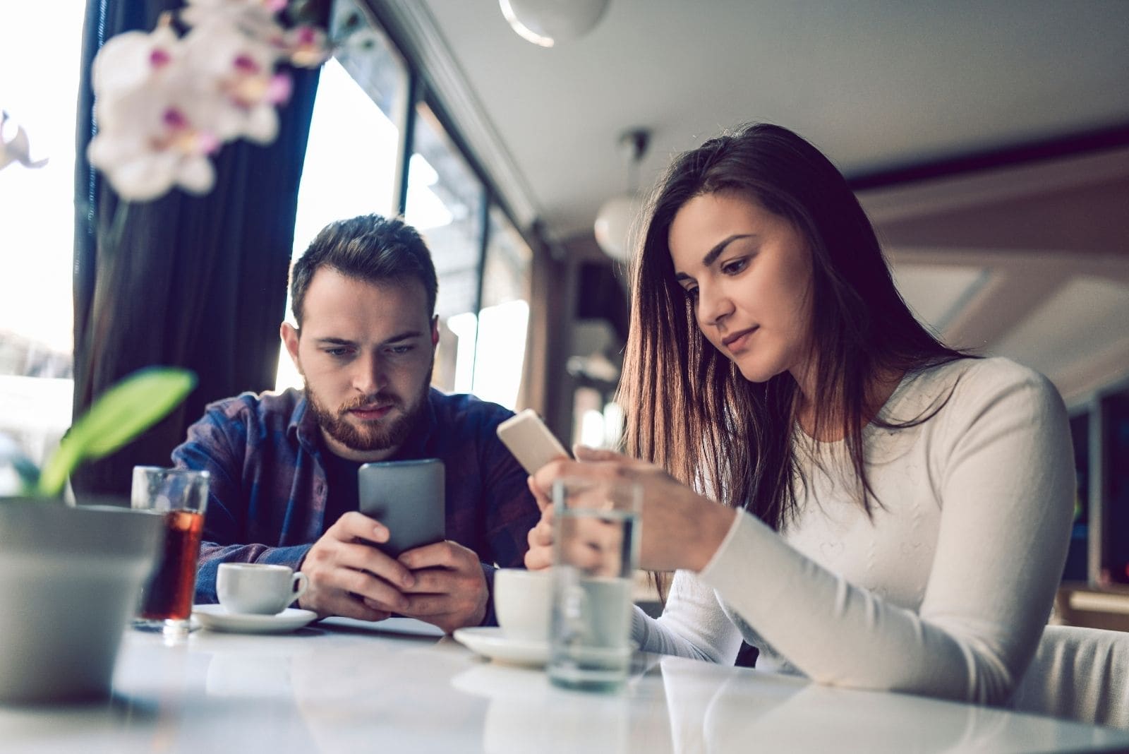 coppia che trascorre il tempo insieme in un silenzio imbarazzante all'interno del caffè, entrambi occupati con i loro gadget