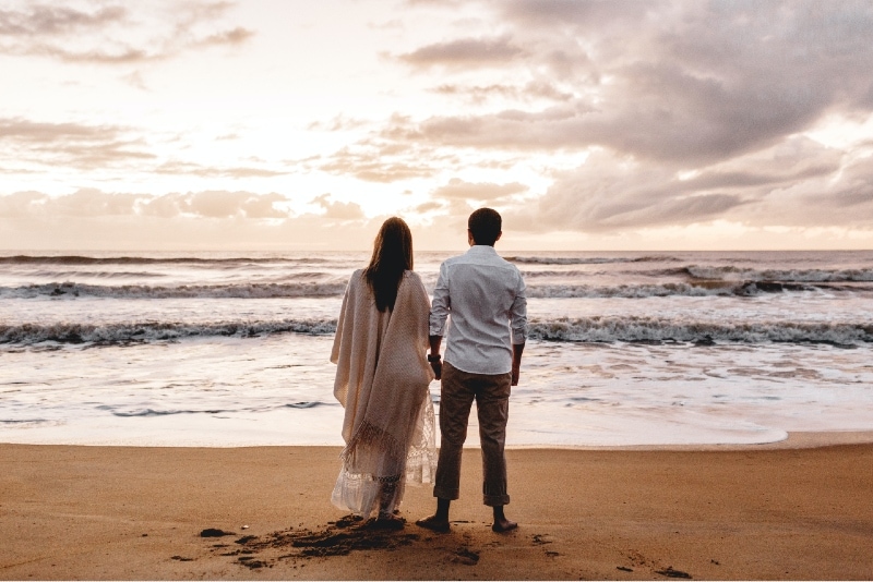 man and woman holding hands while standing on beach