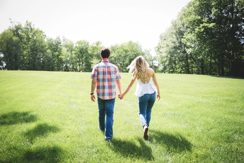 man and woman holding hands while walking on green grass