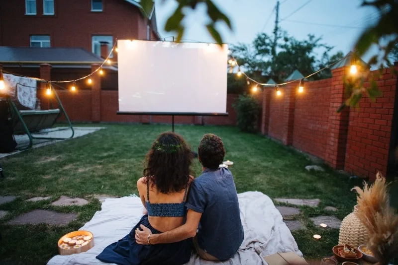 man and woman watching movie on projector screen outdoor