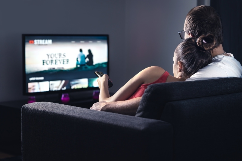 man and woman watching tv while sitting on couch
