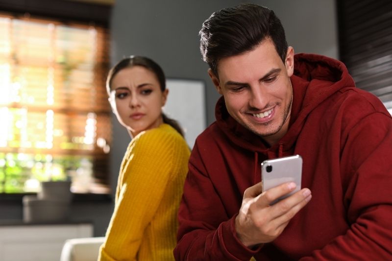 distrust woman peering thru her boyfriends cellphone with jealousy sitting indoors