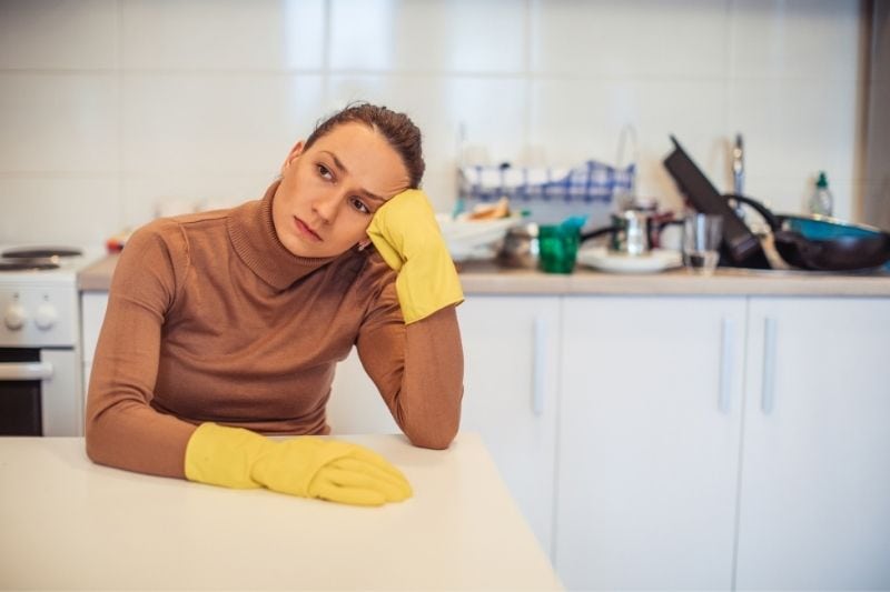 a mulher exausta, de luvas, sentada à mesa da cozinha