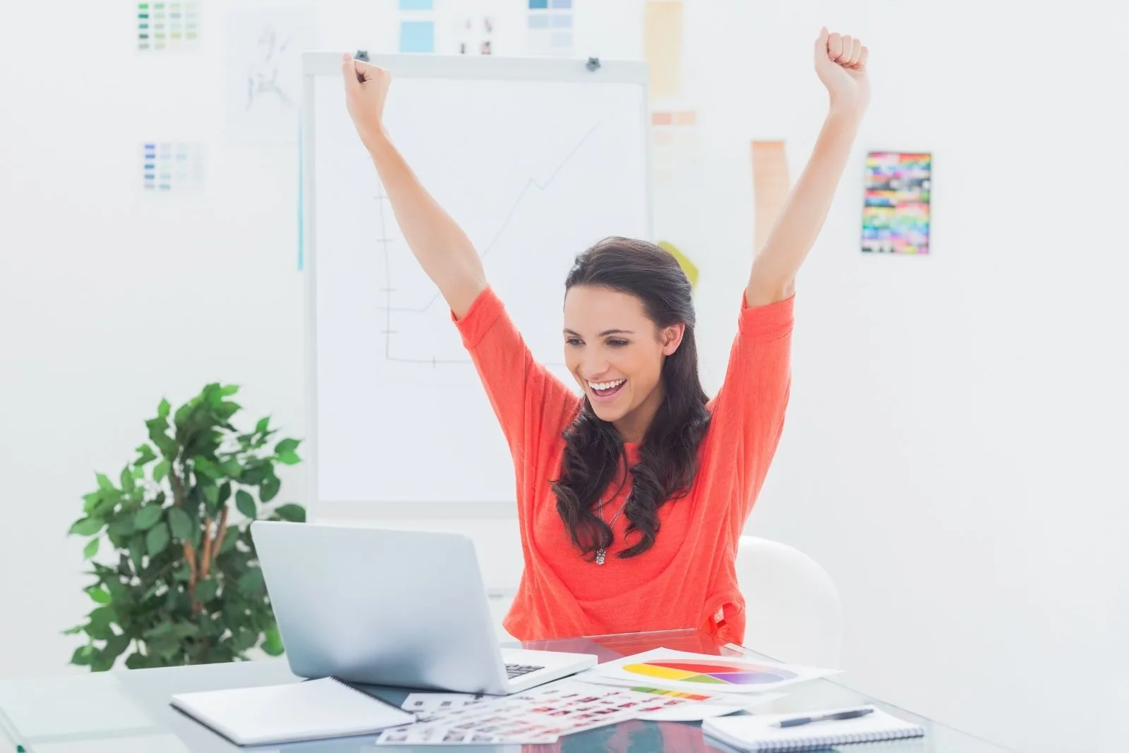 feeling accomplished woman raising her hands while looking at her laptop in her office table
