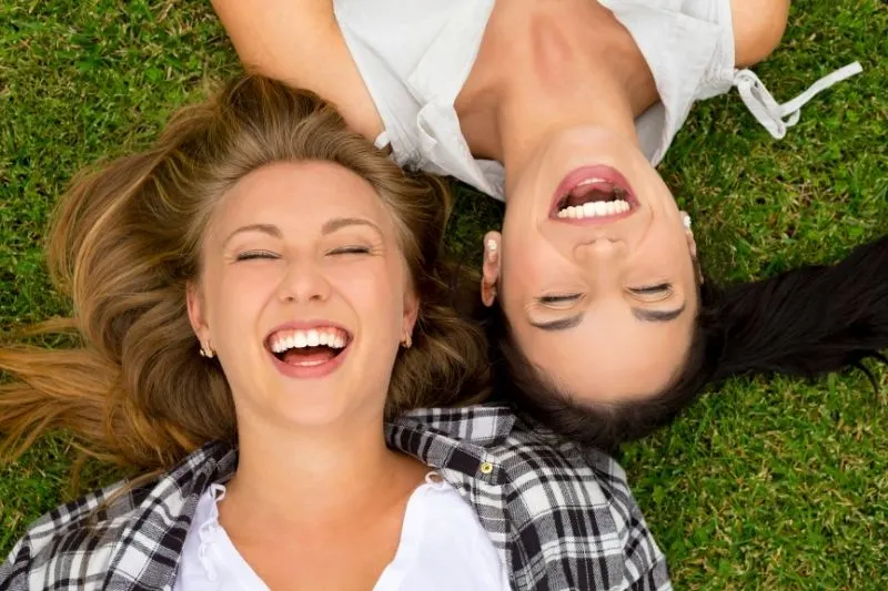 female best friends laughing and lying on the green grasses