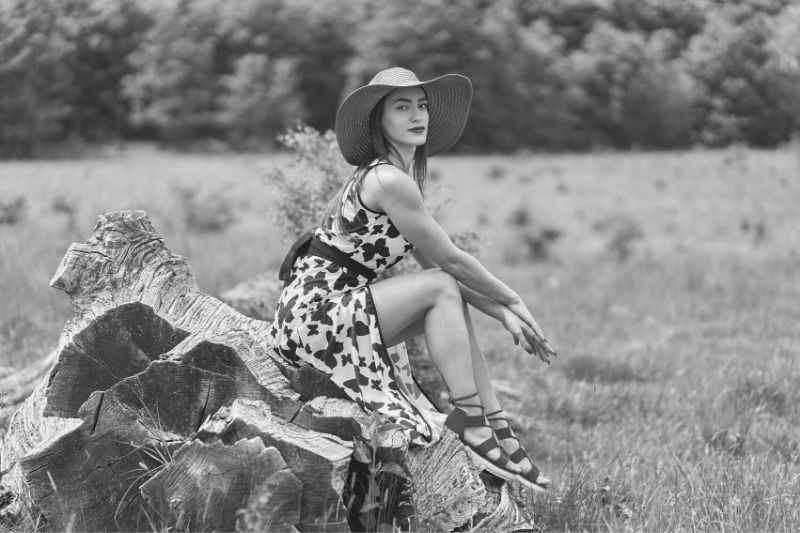 splendida modella in posa all'aperto con cappello seduta su una roccia