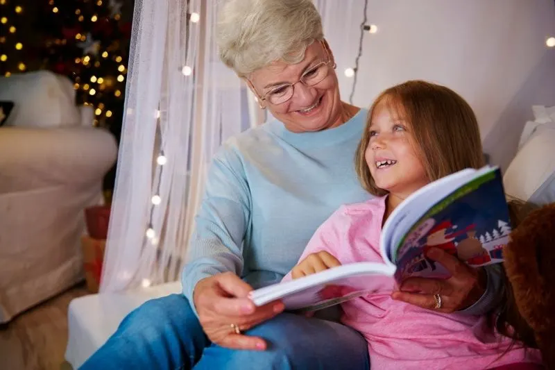 grandmother and granddaughter having good time reading book in the bedroom