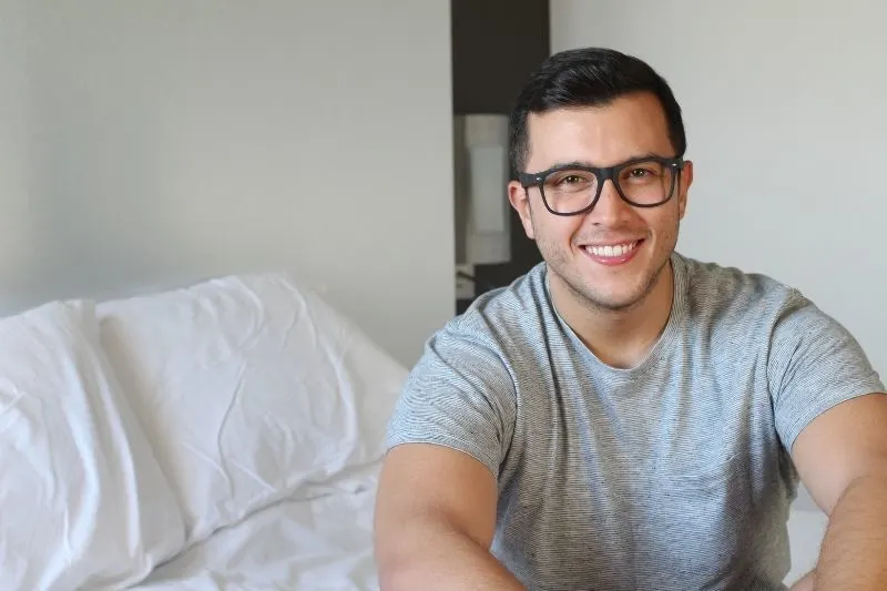 handsome ethnic man smiling at home sitting on bed