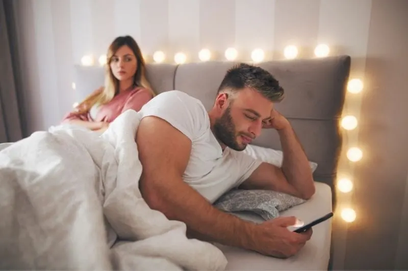 handsome man cheating on his girlfriend hiding his phone while lying in bed