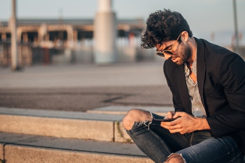 handsome man in black jacket texting in smartphone sitting outdoors