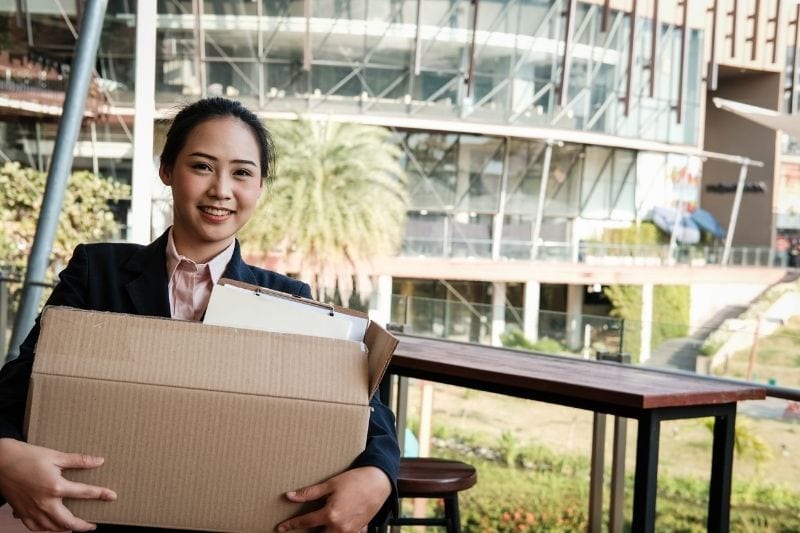 mujer feliz que dimite llevando sus efectos personales en la caja durante su último día