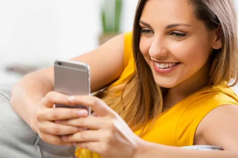 happy woman texting while sitting on sofa smiling