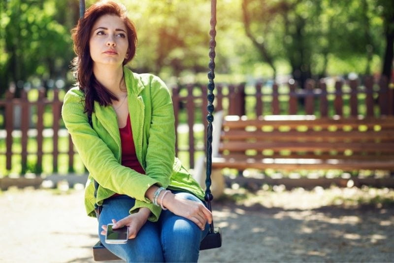 insecure woman sitting in the swing of the park deeply thinking