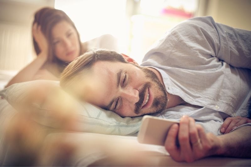 jealous woman looking at his husband texting in bed