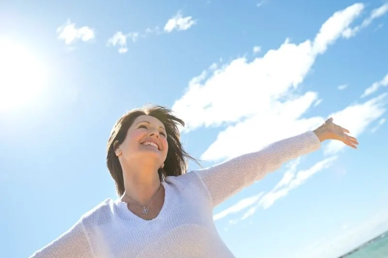 joyful mature woman spreading her arms outdoors with blue and cloudy skies