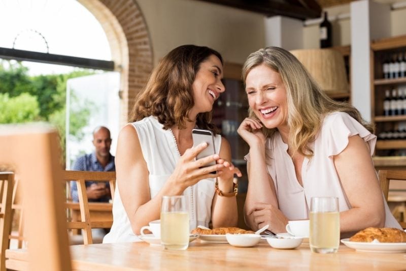 laughing mature friends inside the cafe showing the smartphone 
