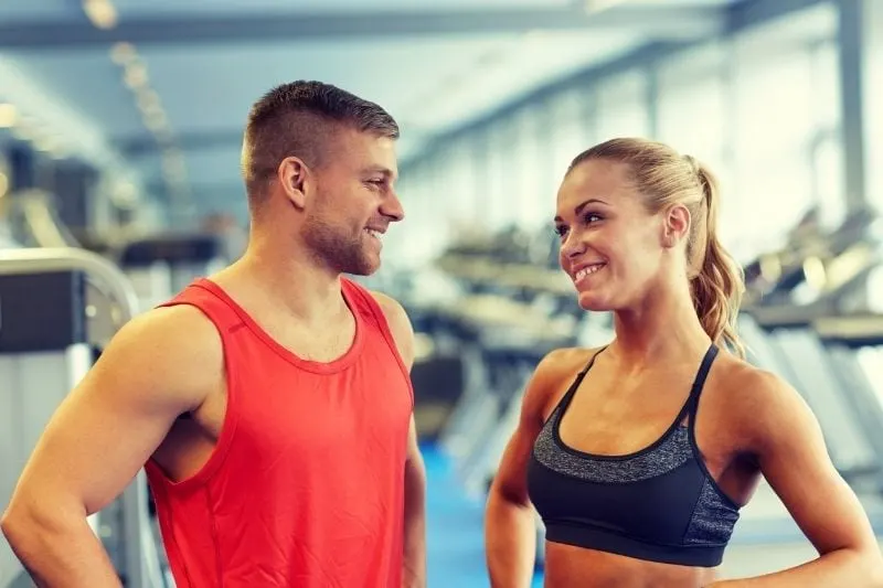 man and woman in gym talking and smilling wearing athletic wear