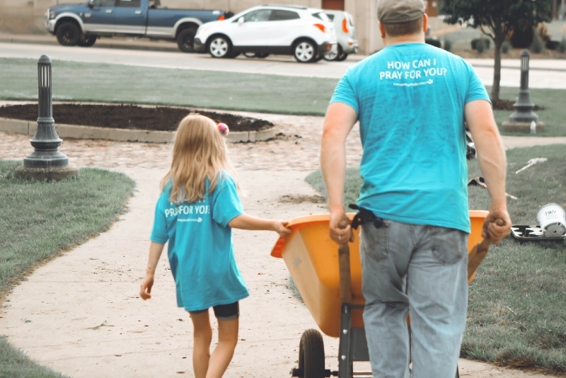 man in blue t-shirt carrying orange wheelbarrow