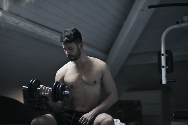 strong man exercising with dumbbell while sitting indoor