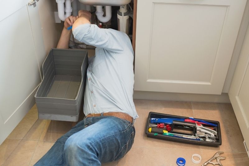 man fixing plumbing under the sink of the kitchen