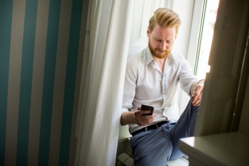 l'uomo si nasconde sotto la tenda rispondendo al telefono che si trova sul davanzale della finestra