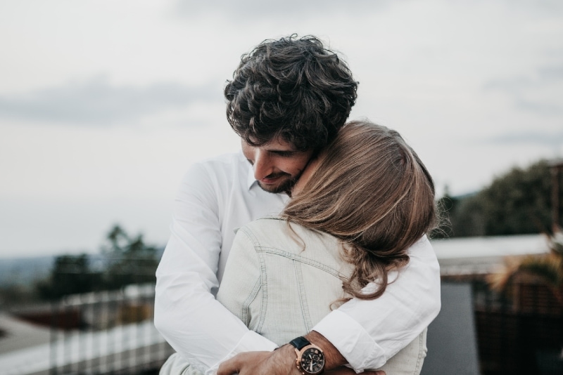 hombre con camisa blanca abrazando a mujer al aire libre