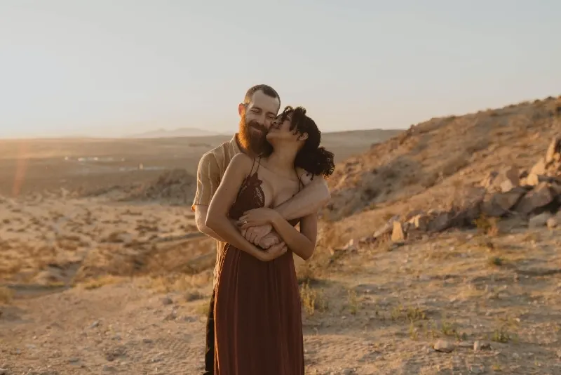 man with beard hugging woman during sunset