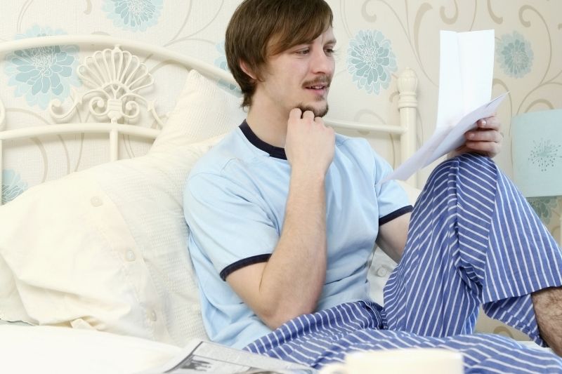 uomo in pigiama che legge una lettera a letto sorridendo