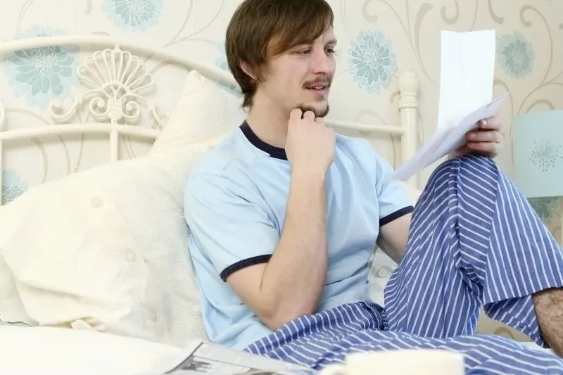 man in pajamas reading a letter in bed smiling