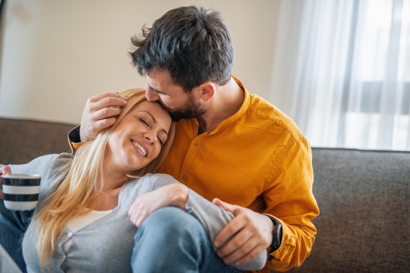man kissing woman's forehead while sitting indoor