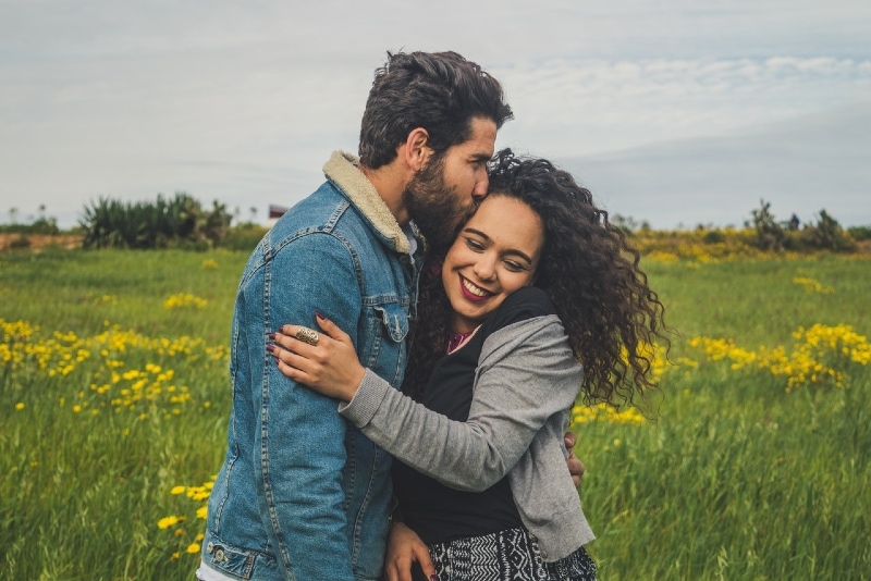 man in denim jacket kissing woman with curly hair