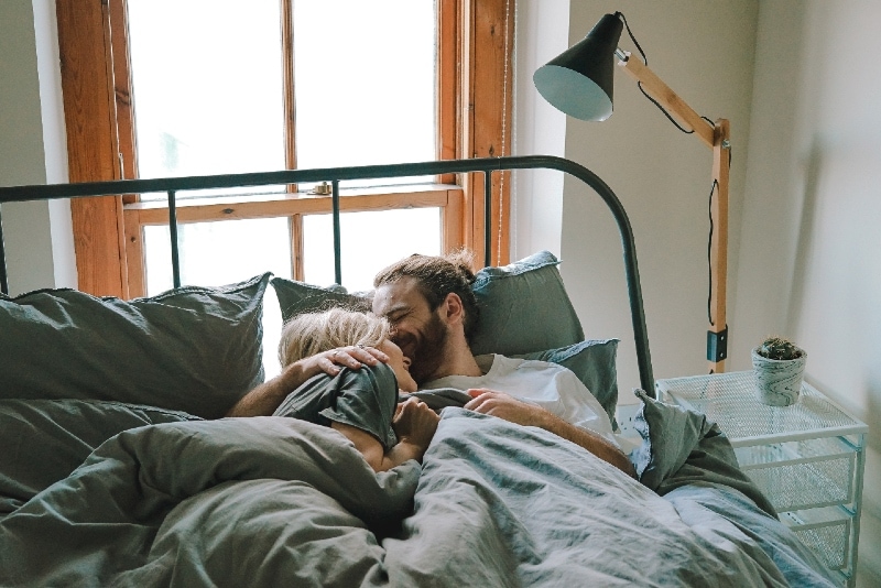 man kissing woman while lying on bed
