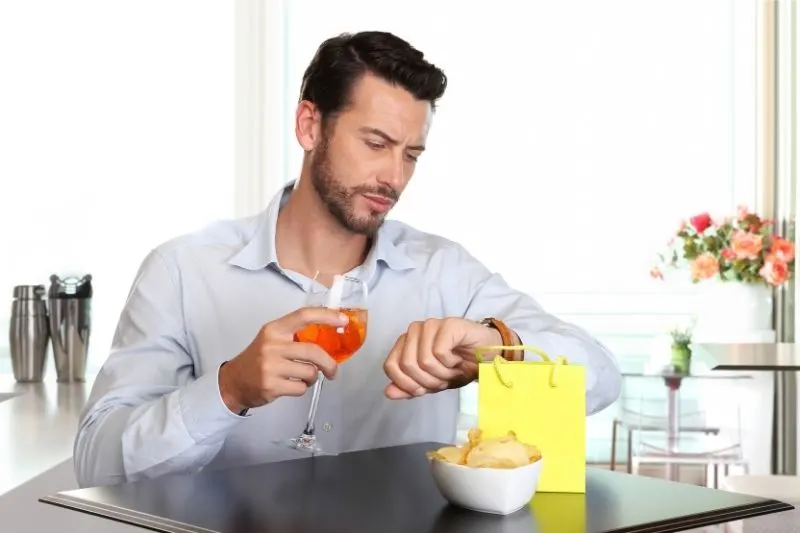 man looking at his watch while sipping a drink inside a restaurant