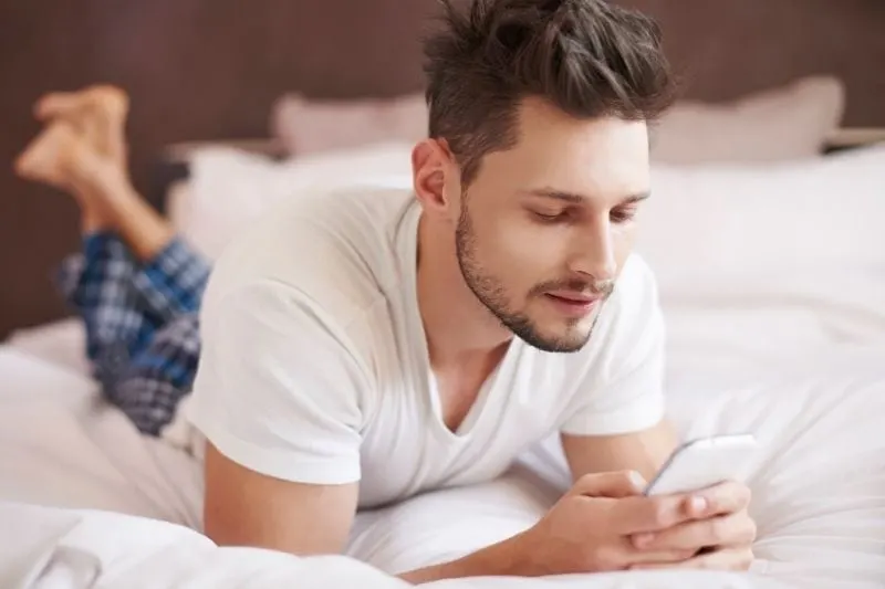 man lying down on bed reading text message from cellphone