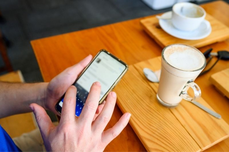 uomo al telefono che posta sui social media all'interno di un bar in un'immagine ritagliata