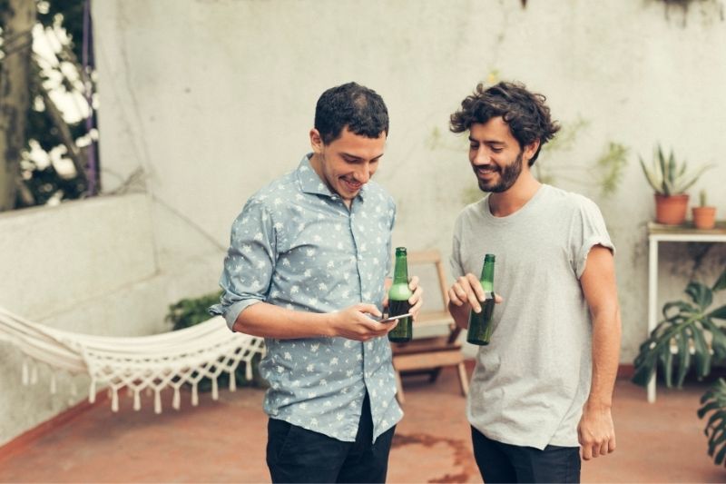 hombre compartiendo número en su teléfono a un amigo mientras bebe cervezas al aire libre