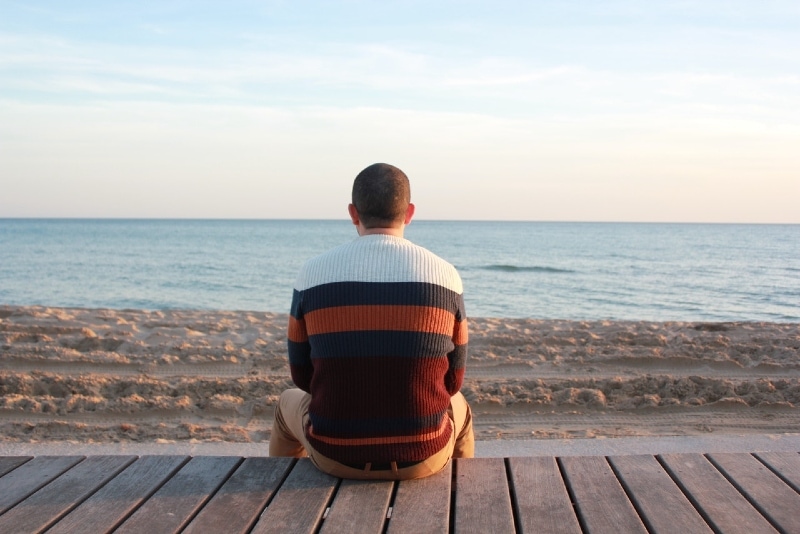 man sitting on wooden panel looking at sea